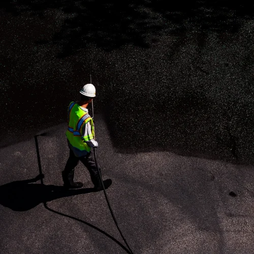 A worker is seen sealcoating a parking lot from overhead