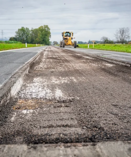 Close-up of textured grinded asphalt with motorized grader at road renovation site
