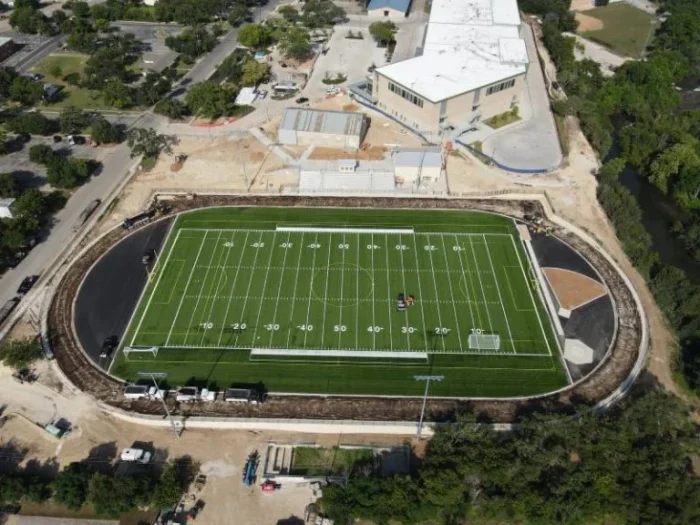 A football field receives a new asphalt track around it.